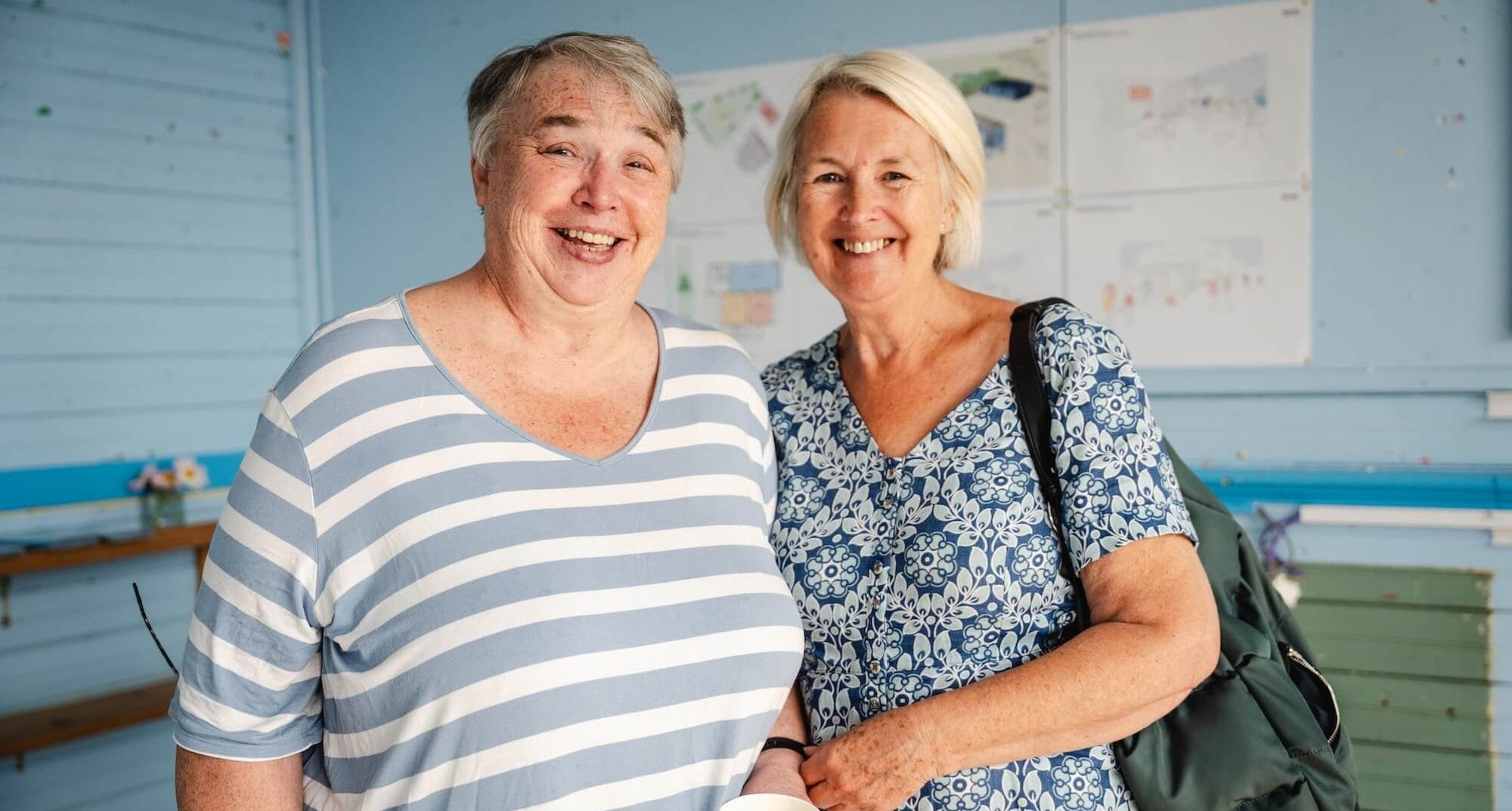 2 ladies smile at camera wearing blue in a blue room